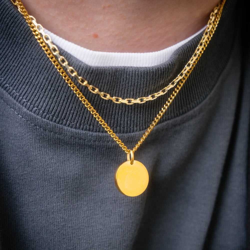 Gold chain necklace with a round pendant worn by a person against a dark sweater background