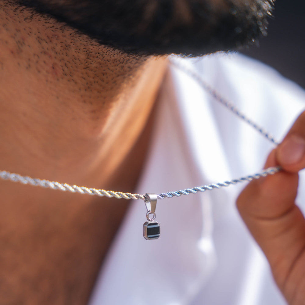 Close-up of a silver necklace with a pendant held by a person wearing a white shirt.