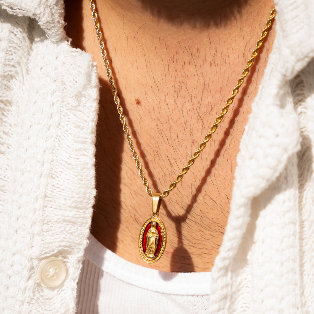Gold necklace with a red pendant worn by a person in a white textured garment.