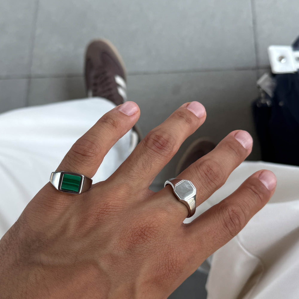 Hand wearing two silver rings with gemstones on a neutral background