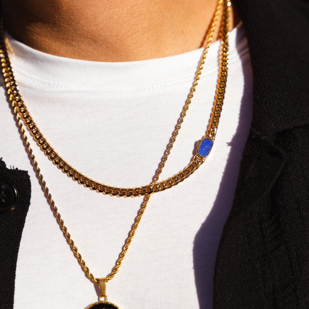 Close-up of a person wearing multiple gold necklaces with pendants on a white background