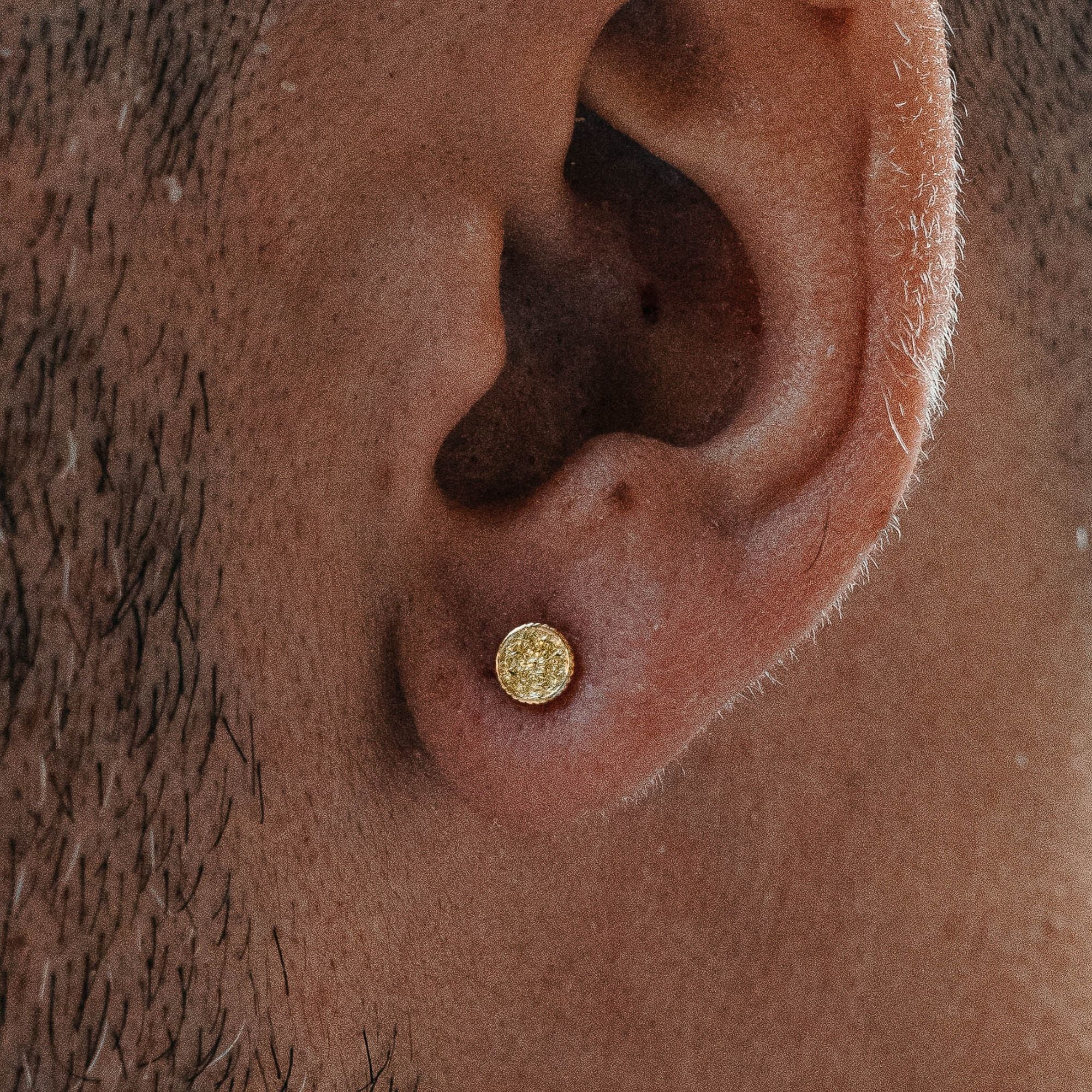 A close-up of a person's ear wearing a small round gold stud earring.