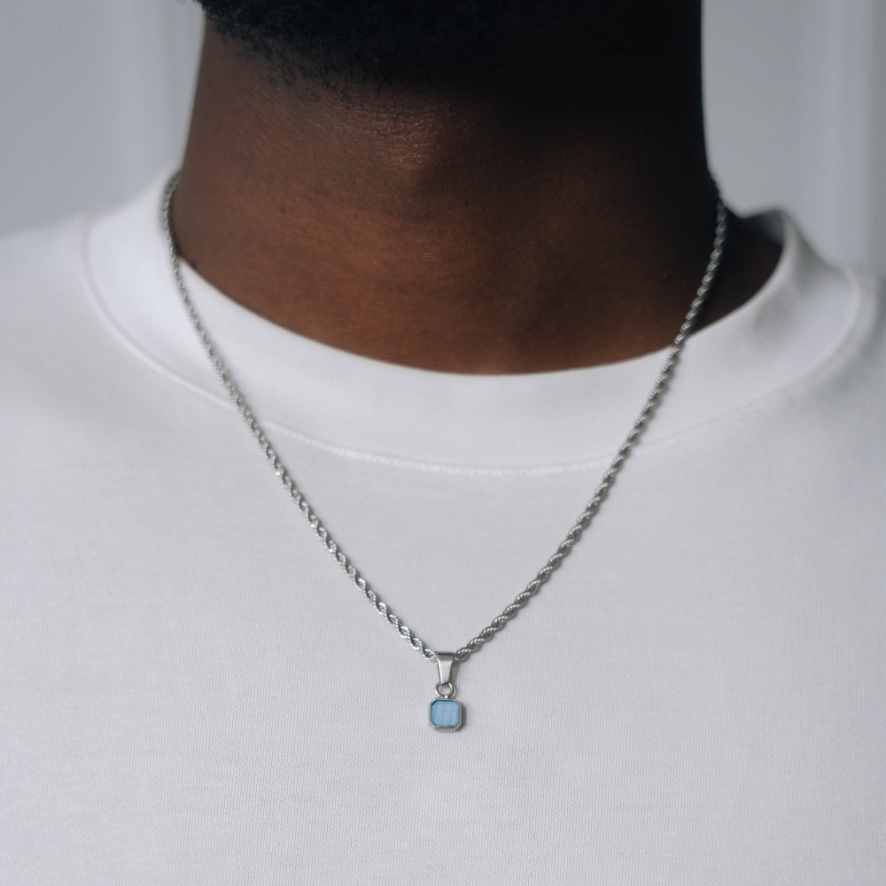 Necklace with a blue pendant worn by a person on a plain background