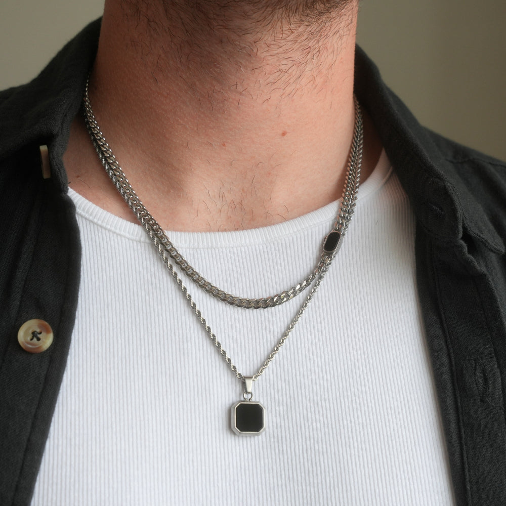 Person wearing a layered chain necklace with a black pendant on a plain background