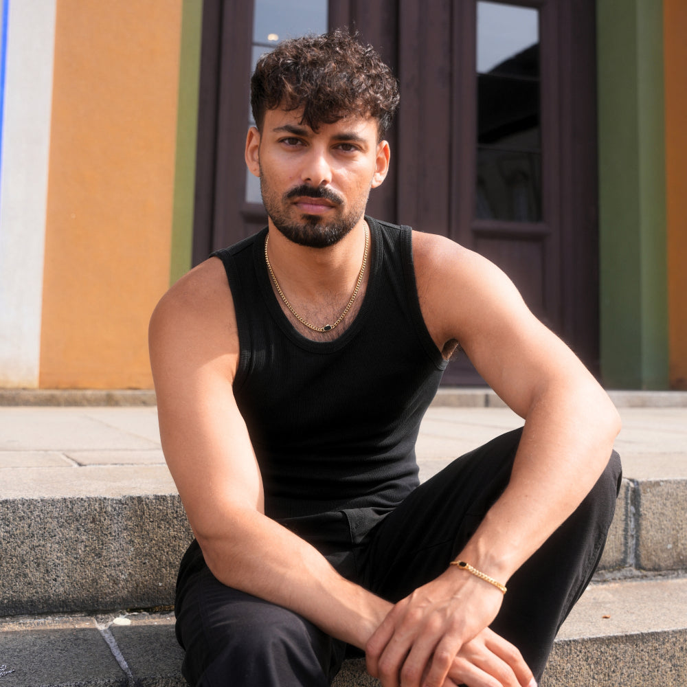 Man sitting on steps wearing a black tank top and pants with a colorful building in the background
