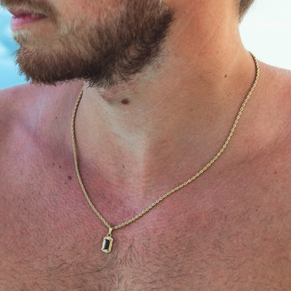 Man wearing a gold necklace with a pendant outdoors