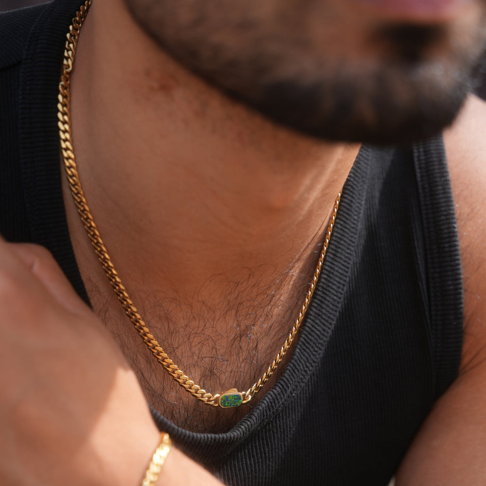 Close-up of a person wearing a gold chain necklace with a small green pendant.
