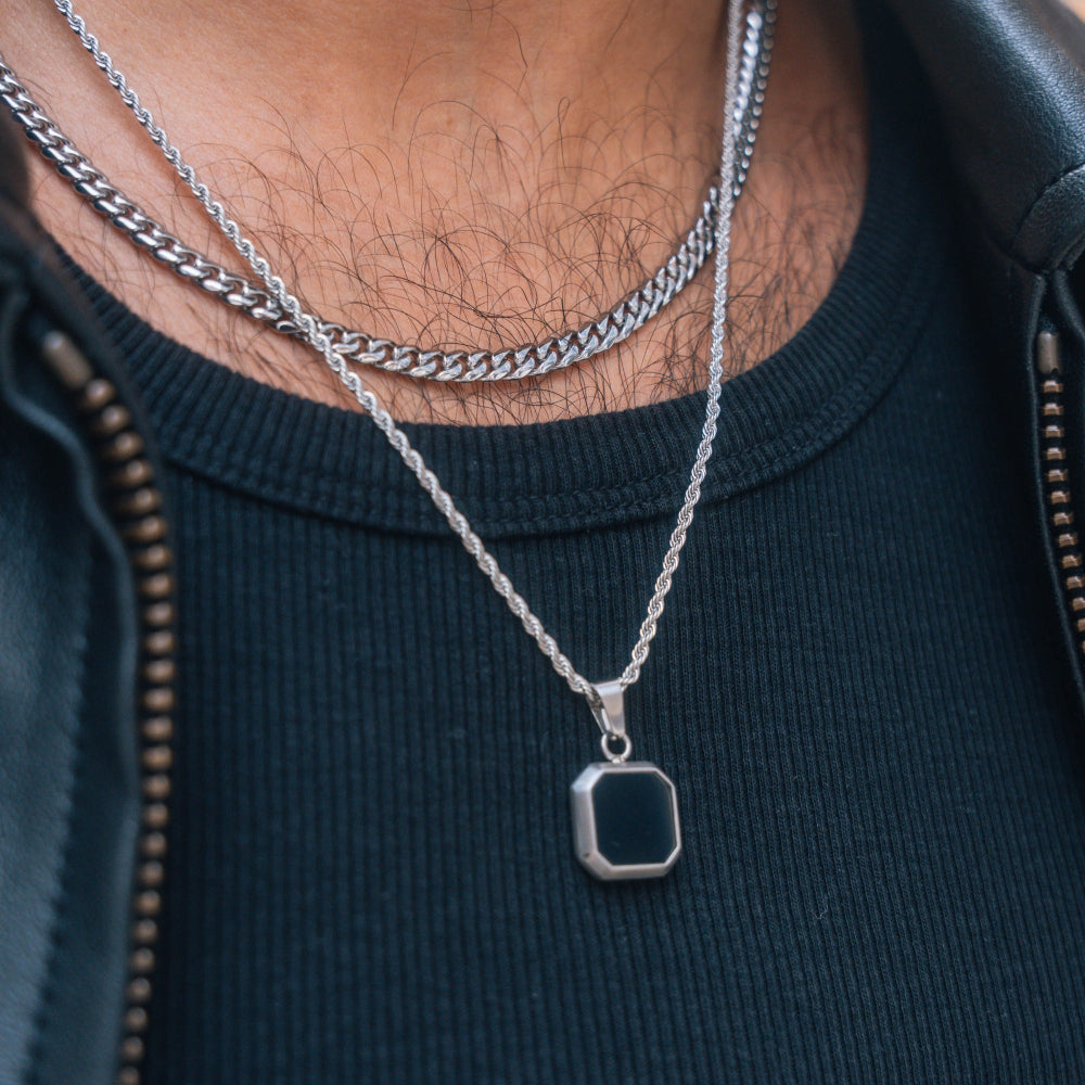 Close-up of a person wearing two silver necklaces with a dark sweater.