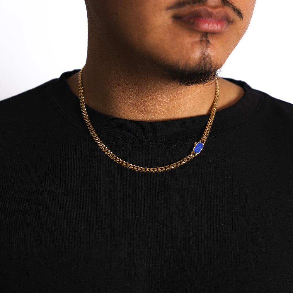 Man wearing a gold chain necklace with a blue pendant on a white background