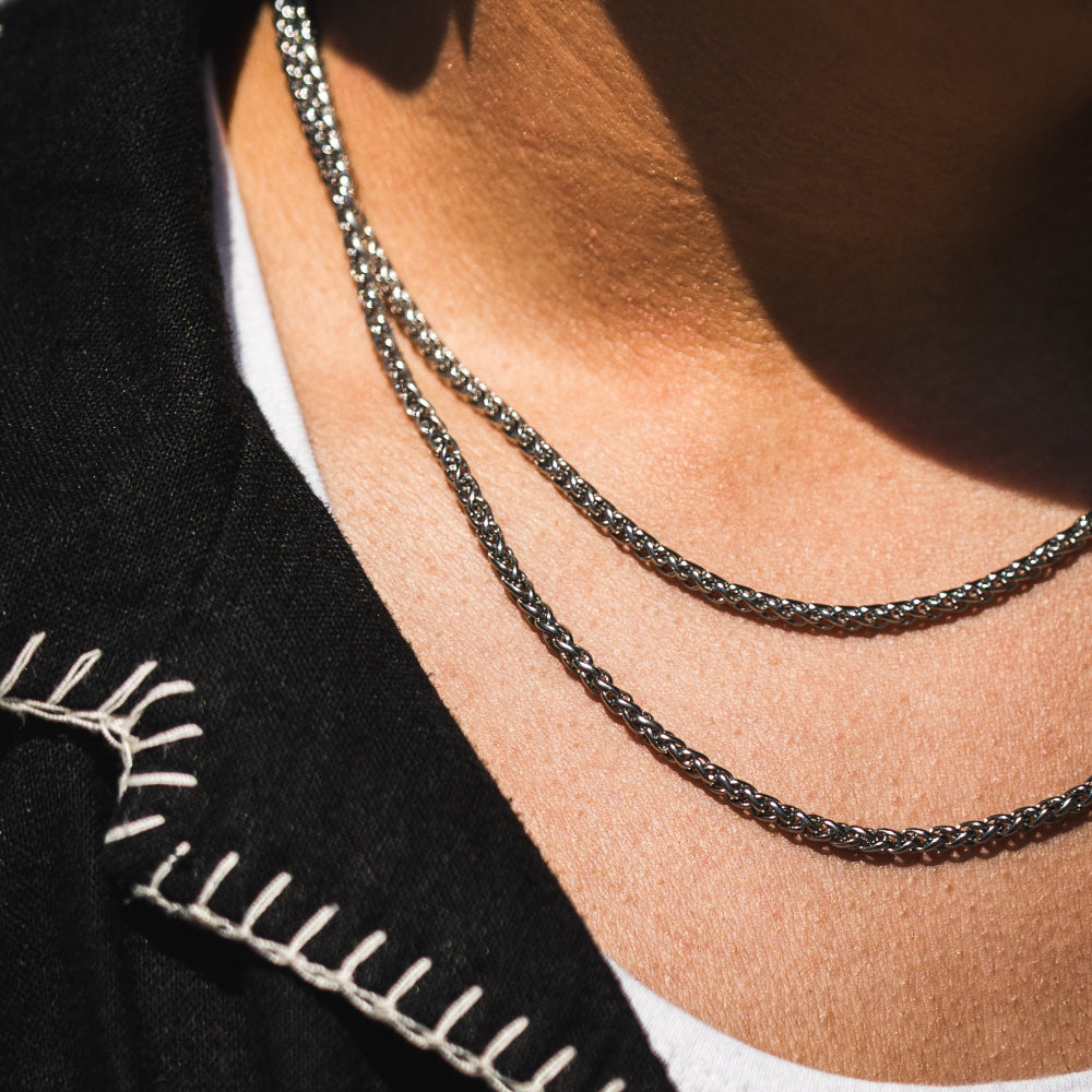 Close-up of a person wearing two silver necklaces with a black garment and white shirt in the background.