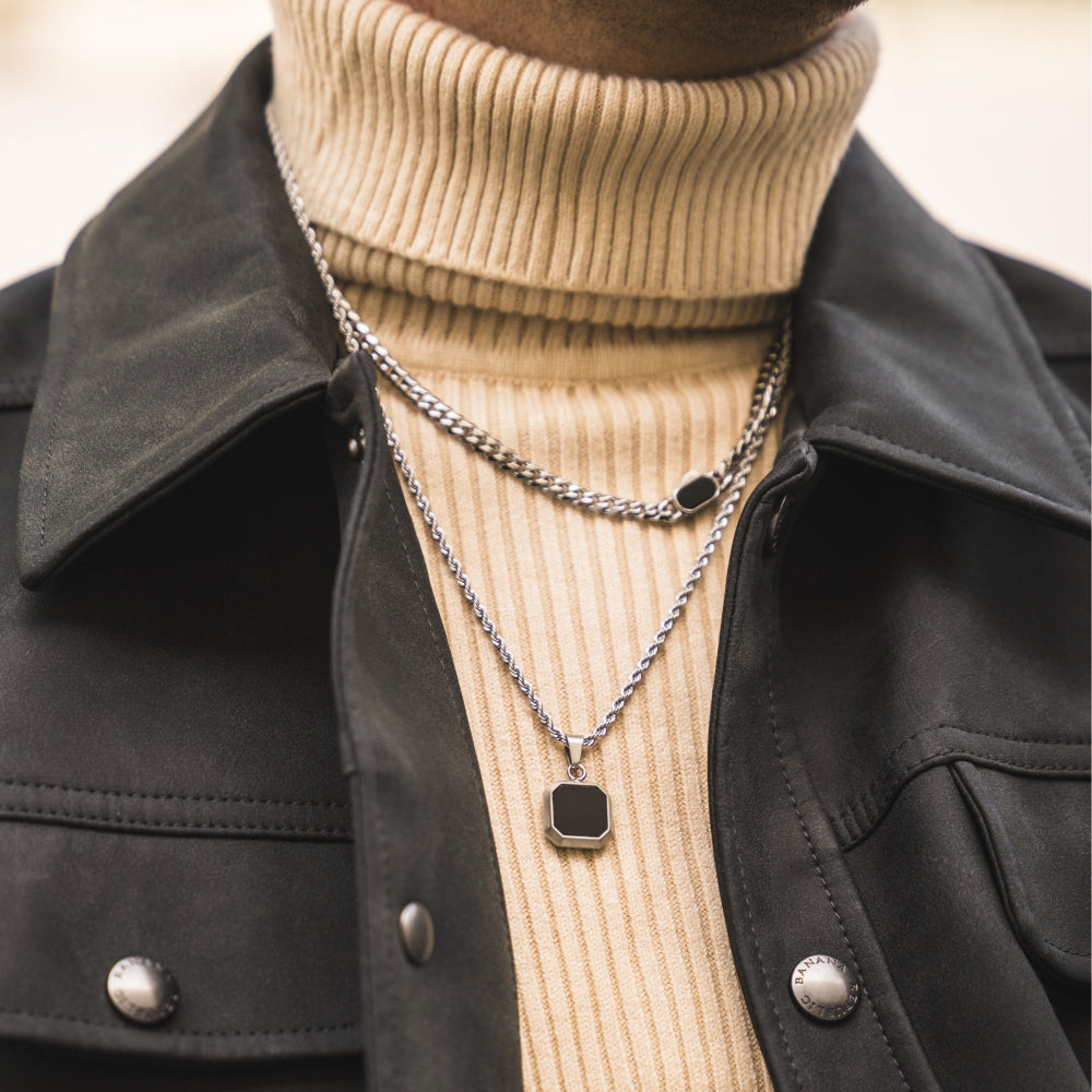 Person wearing a black jacket and beige turtleneck with layered necklaces.