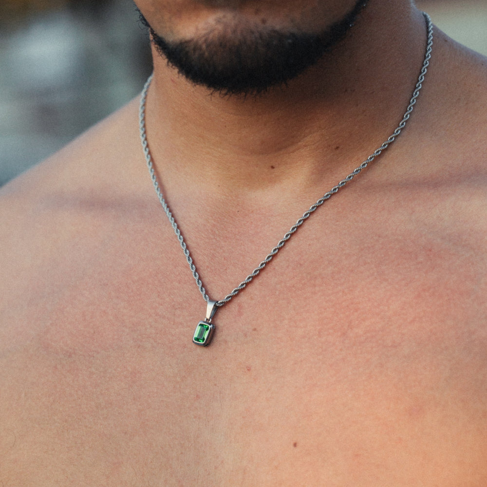 Man wearing a silver necklace with a green gemstone pendant.
