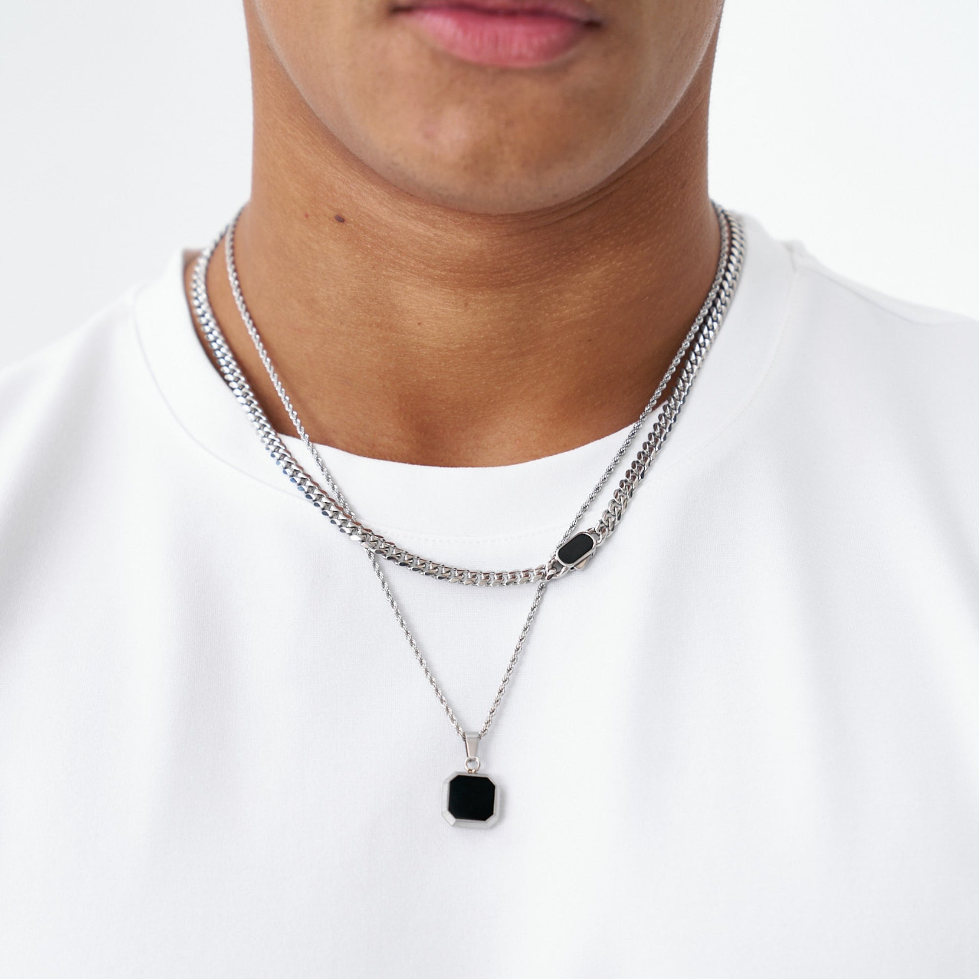 Person wearing a silver necklace with a black pendant on a white background