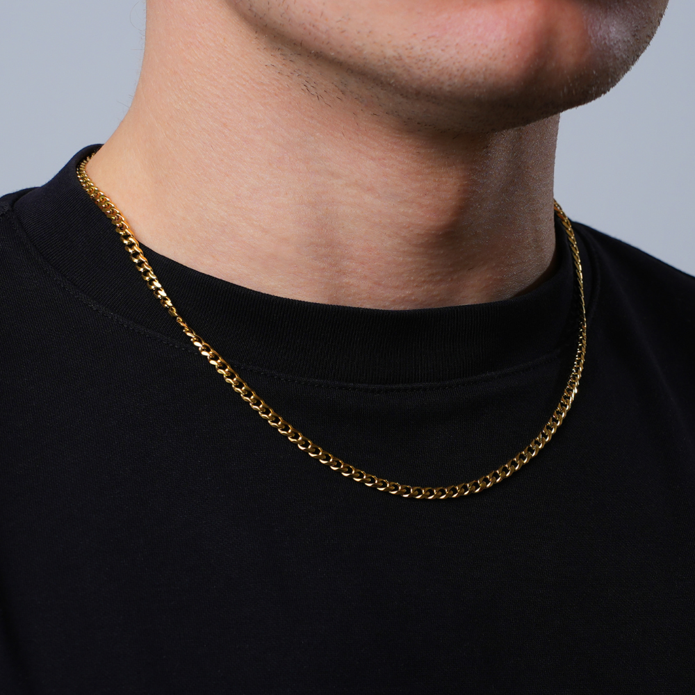 Gold chain necklace worn by a person on a plain background