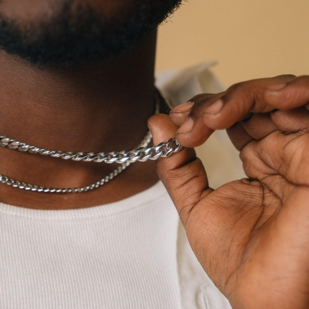Person adjusting a silver chain necklace with a neutral background