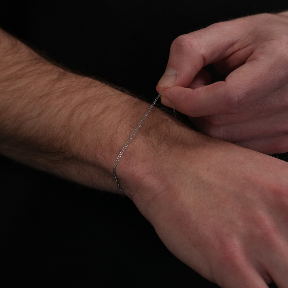 Person wearing a silver chain bracelet on a dark background