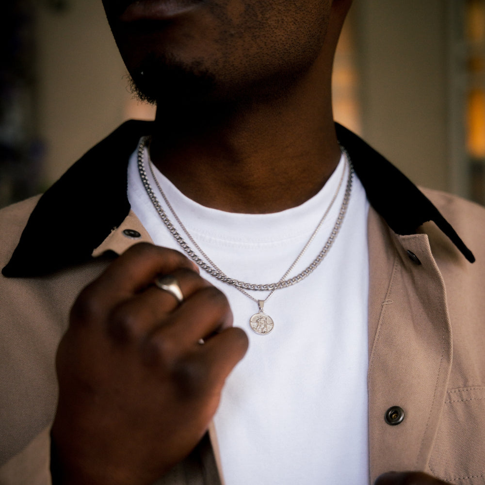 Person wearing a silver necklace with a pendant, close-up of neck and hand.