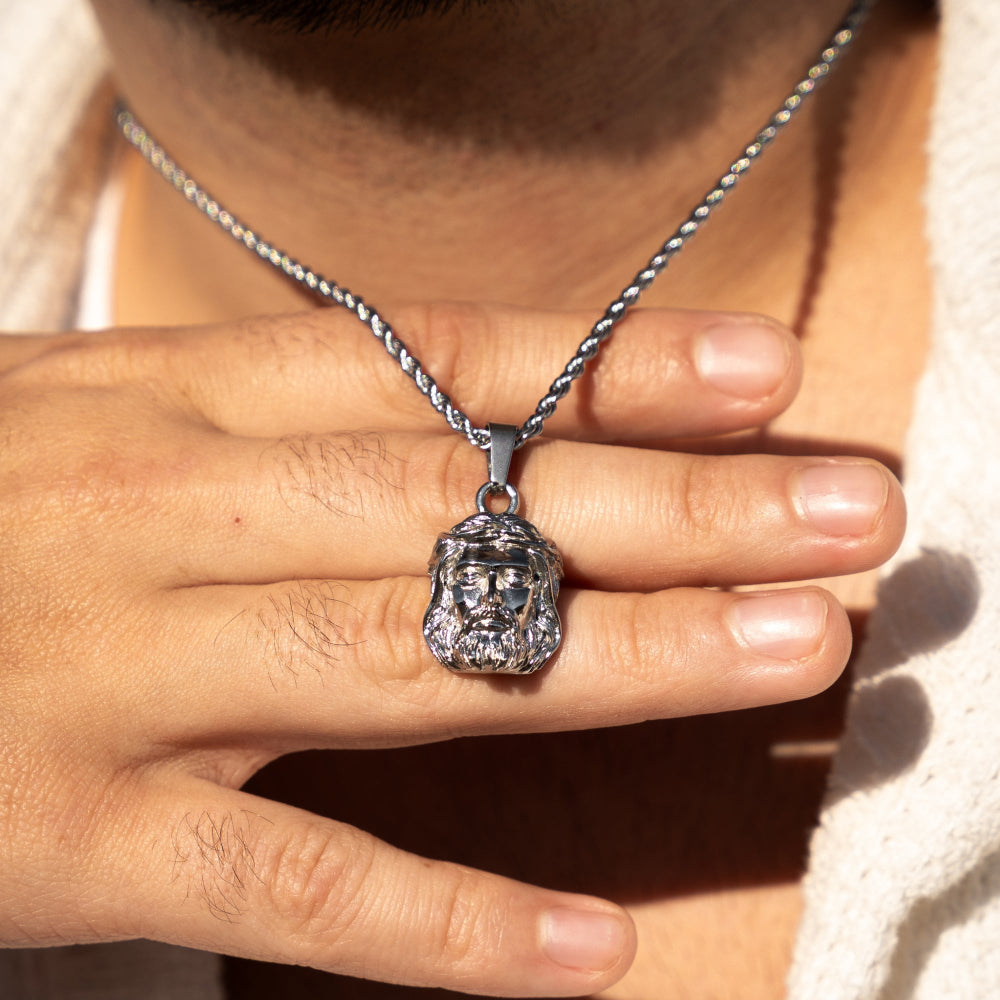 Close-up of a hand holding a silver necklace with a pendant.