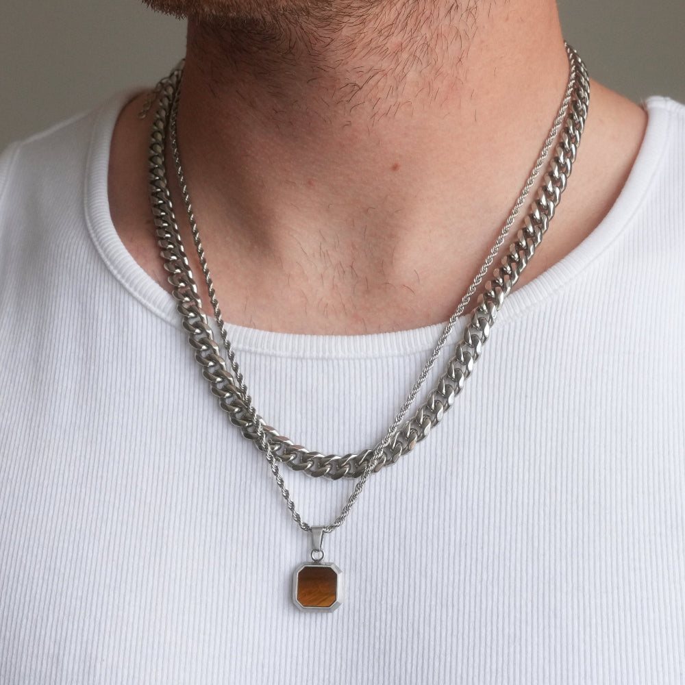 Close-up of a person wearing two silver chain necklaces with a pendant on a plain background