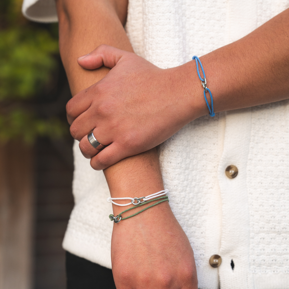 Close-up of a person's arm with multiple bracelets and a ring, wearing a white textured garment.