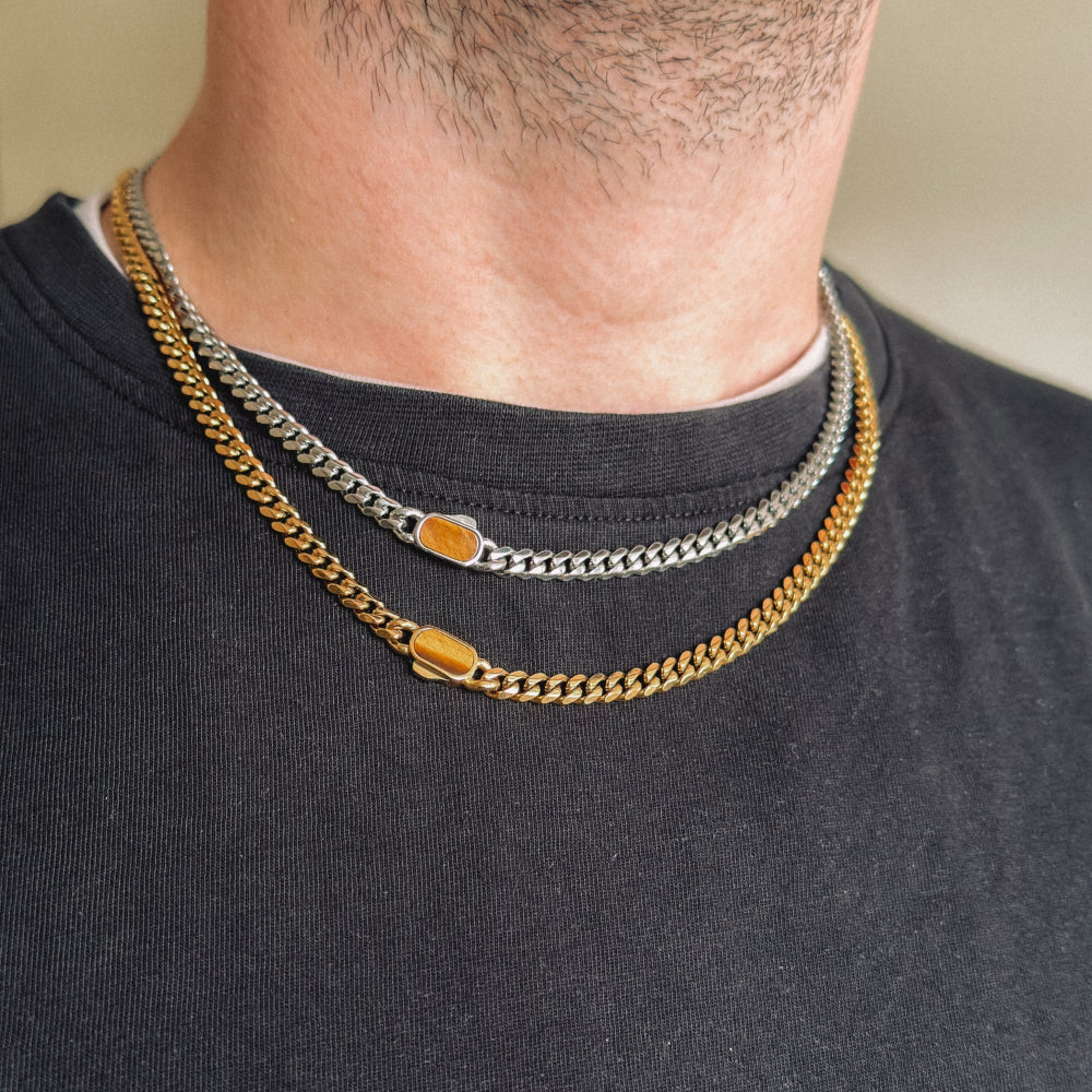 Two gold chain necklaces on a person wearing a black shirt.