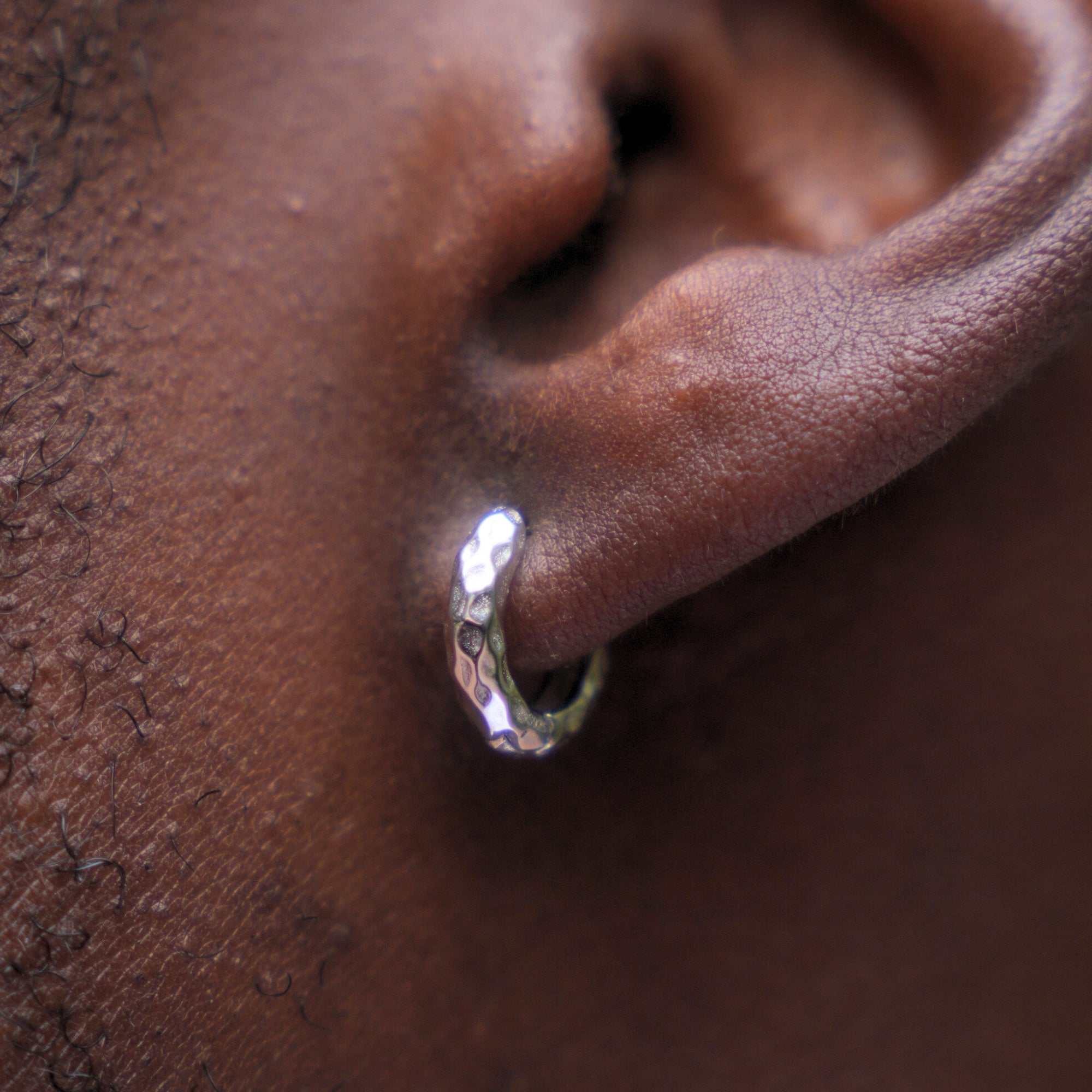 Close-up of an ear with a silver hoop earring on a dark skin background