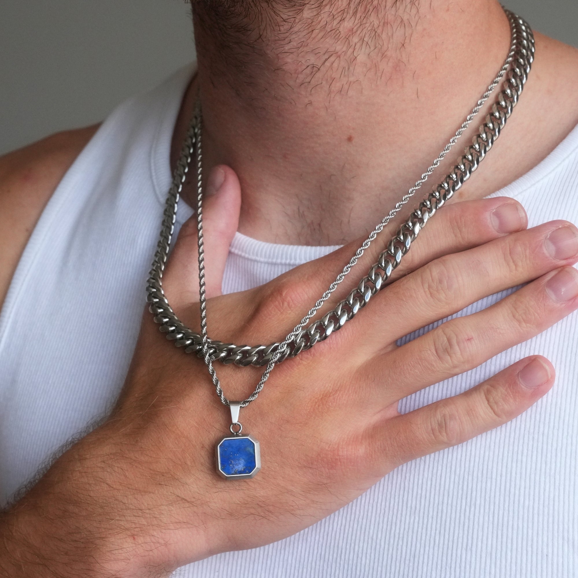 Person wearing a silver chain necklace with a blue pendant on a plain background