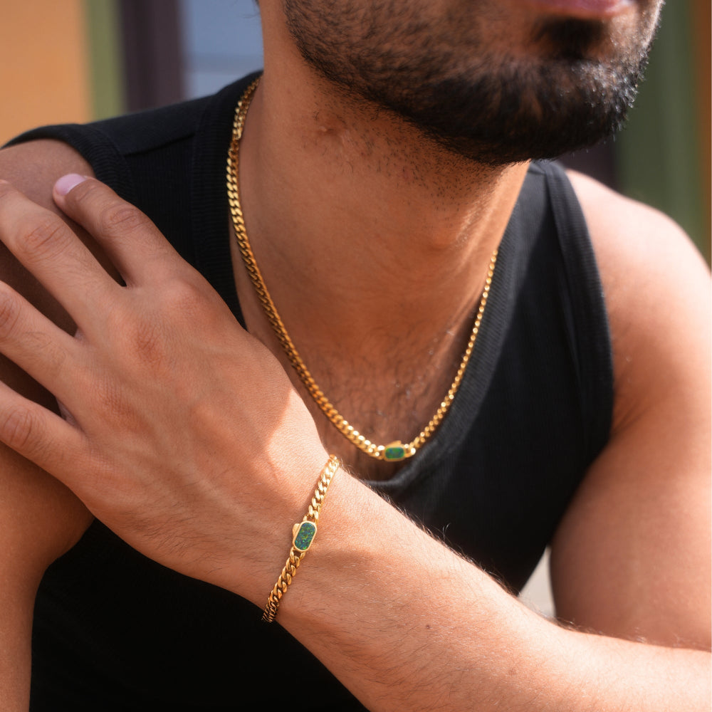 Man wearing a gold chain necklace and bracelet with green stones.