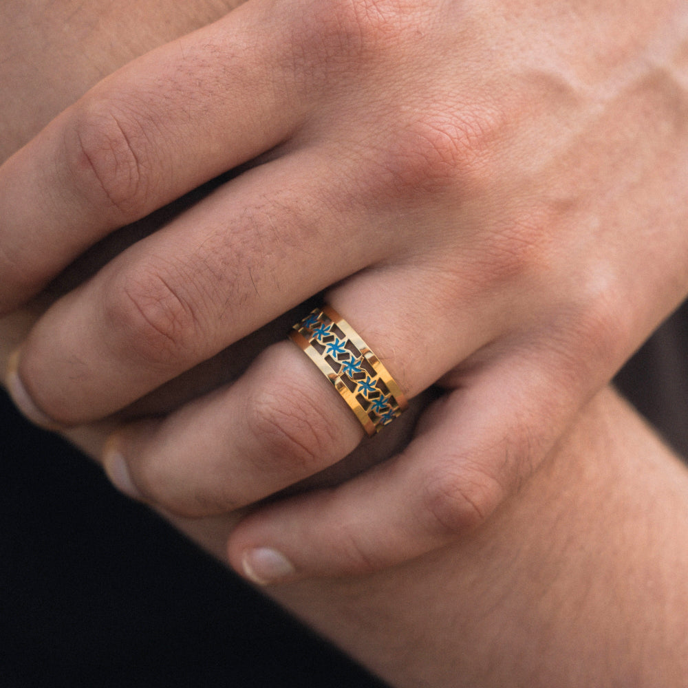 Gold ring with blue stones on a person's finger against a neutral background