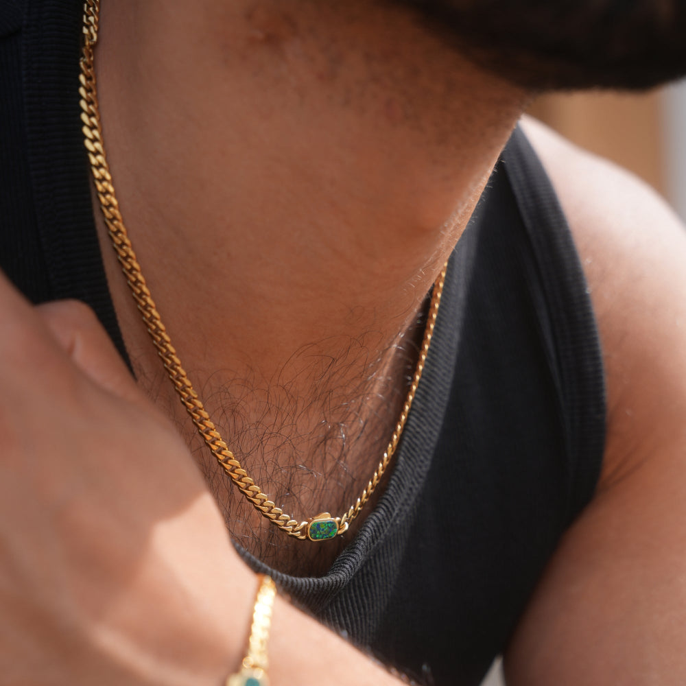 Close-up of a person wearing a gold chain necklace with green gemstones.