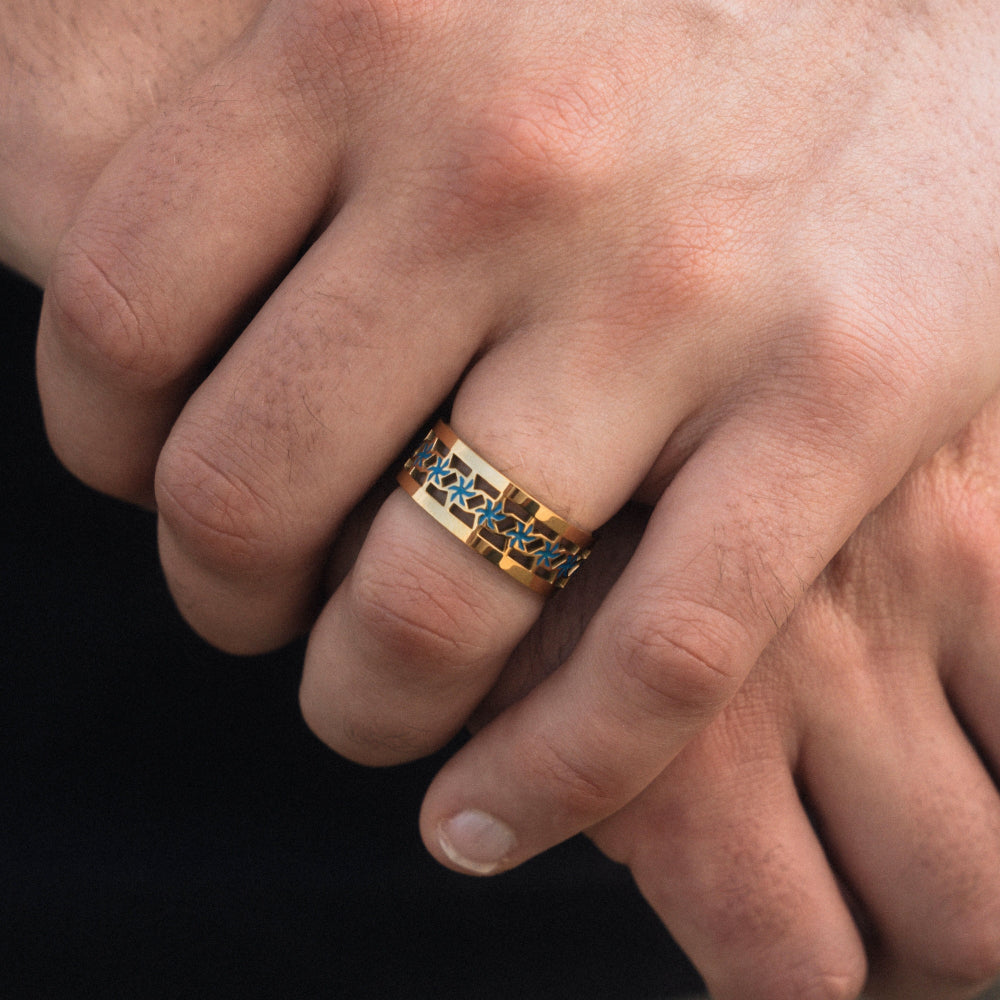 Close-up of a hand wearing a gold ring with blue stones on a black background