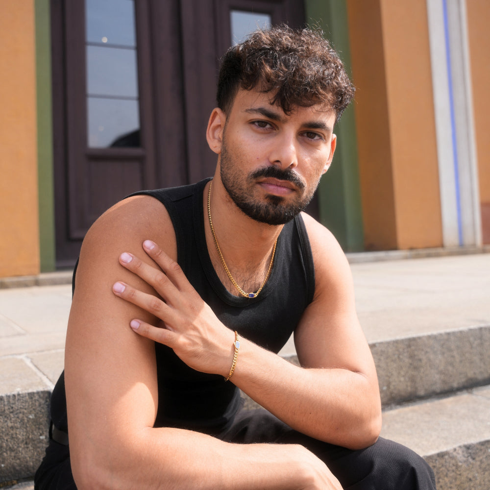 Man sitting on steps wearing a black sleeveless shirt and gold necklace.