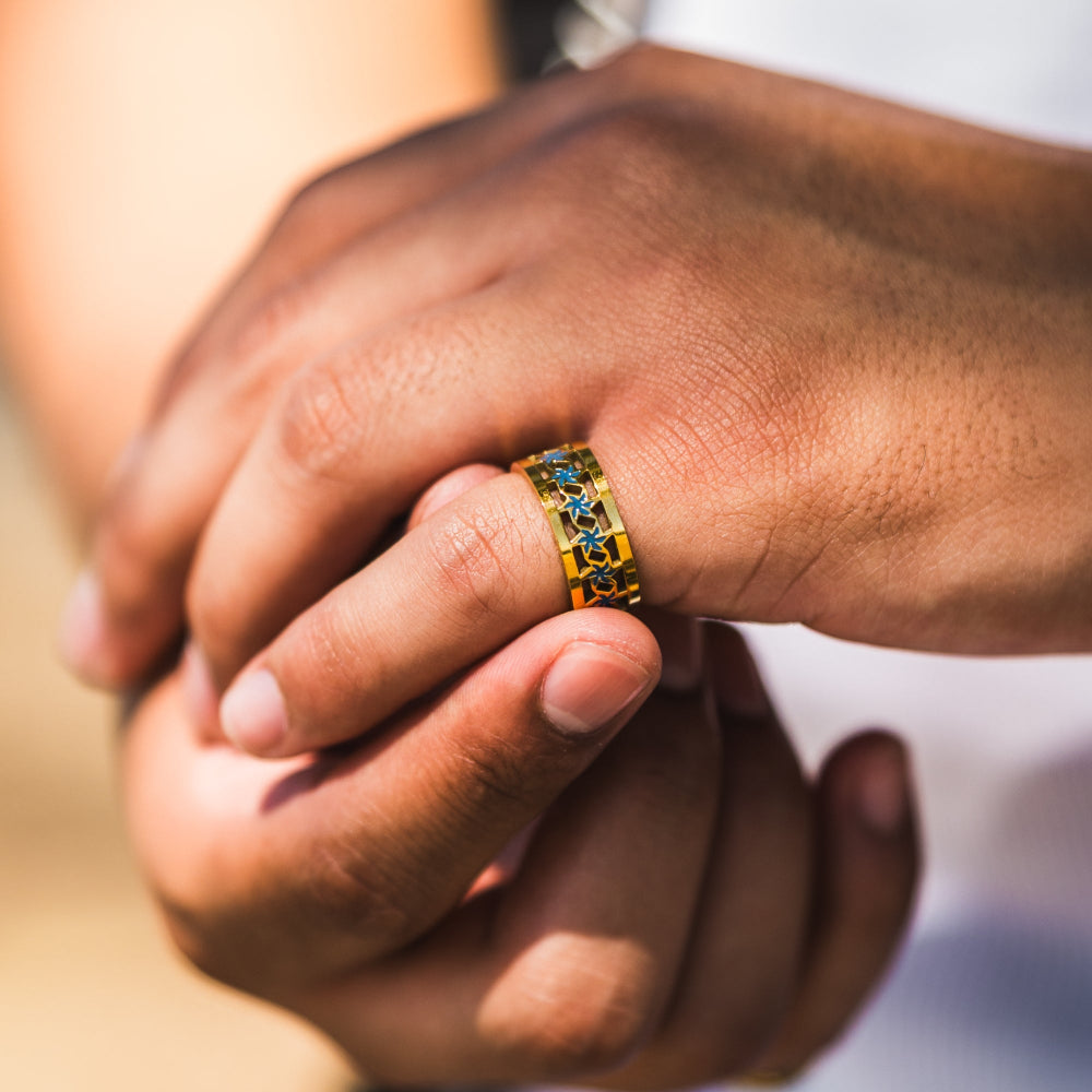 Close-up of a hand wearing a gold ring with blue stones, held by another person.