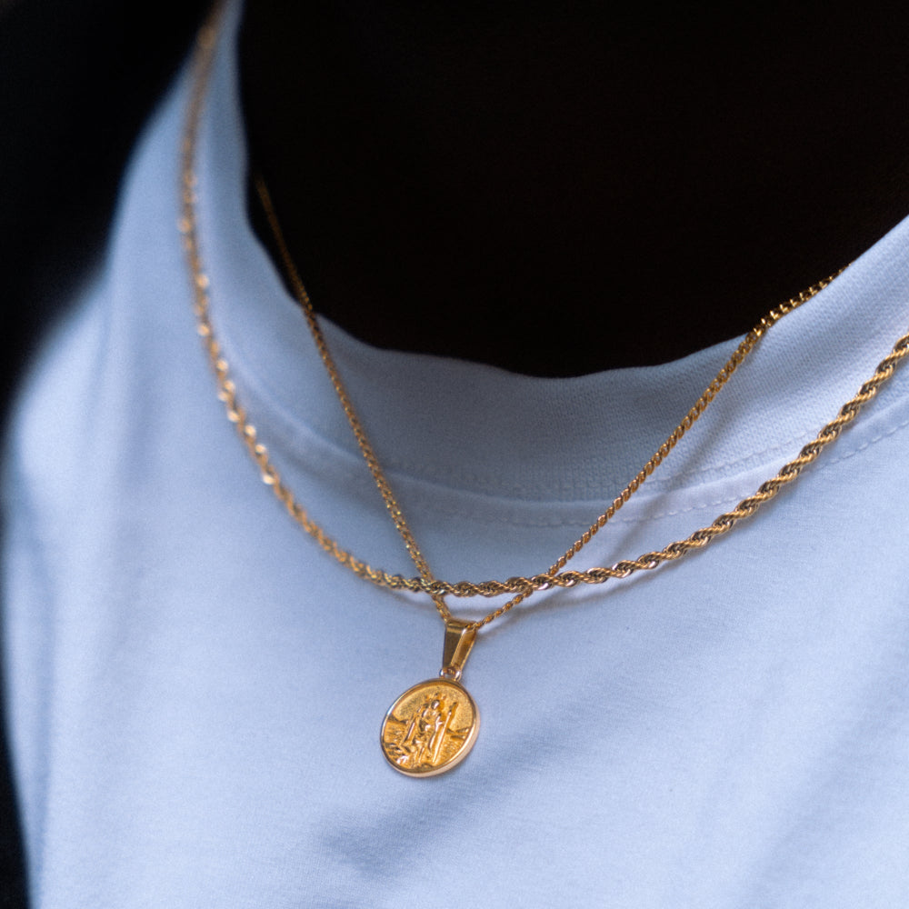 Gold necklace with a pendant on a person wearing a light blue shirt.