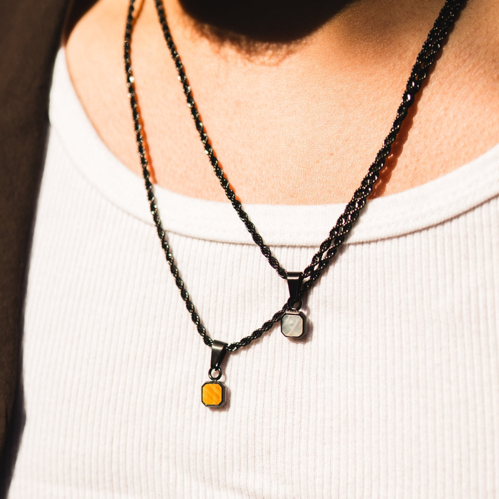 Close-up of a person wearing two black braided necklaces with small pendants.