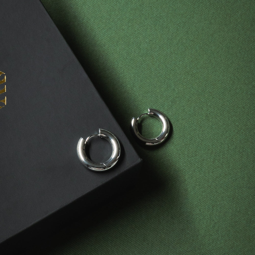 Silver hoop earrings on a dark green surface