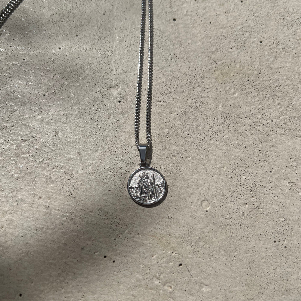 Silver necklace with a round pendant on a concrete surface