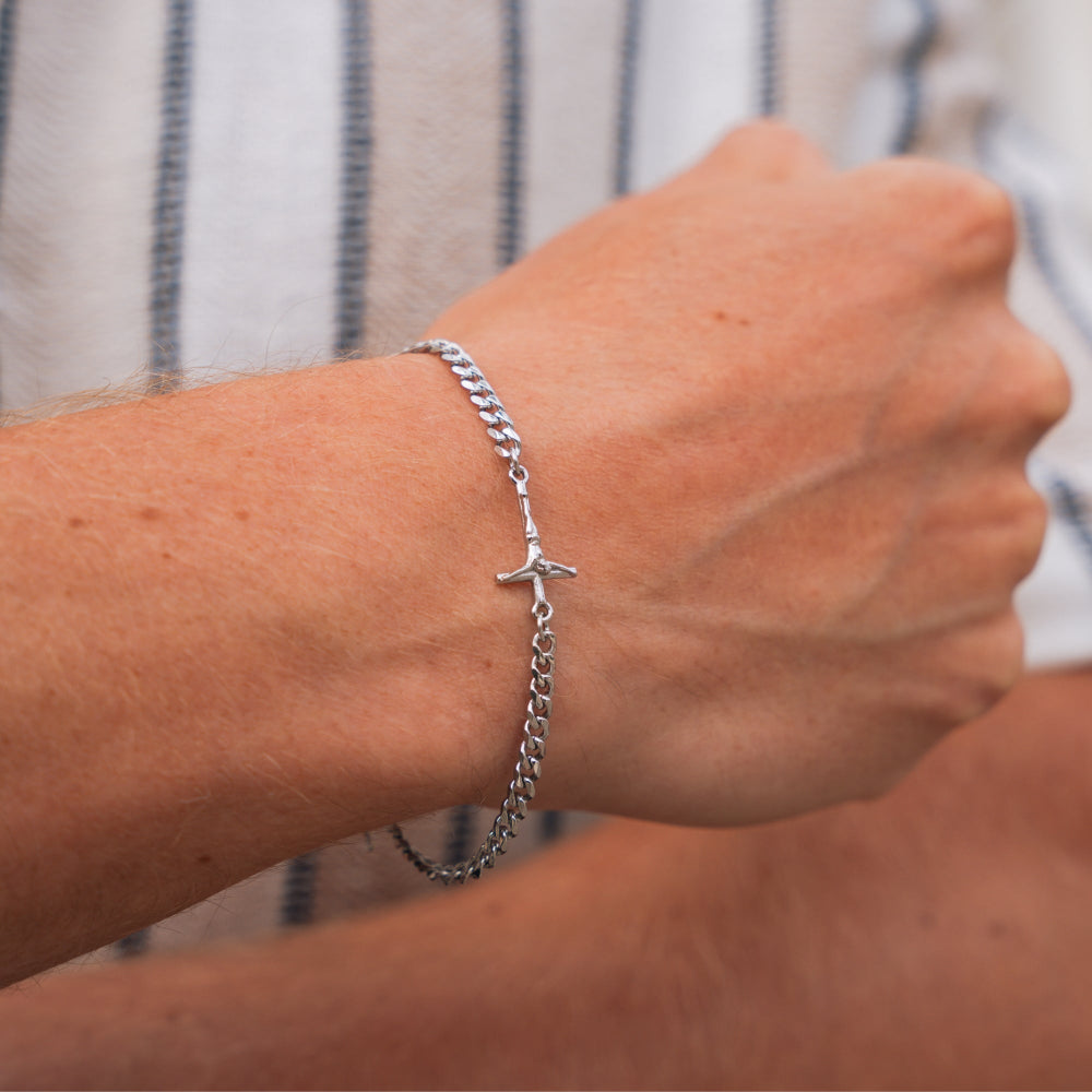 Silver chain bracelet with a cross on a wrist against a blurred background