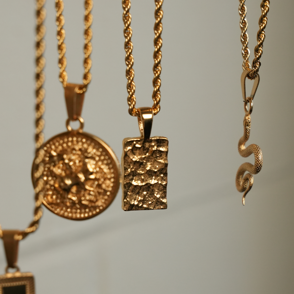 Three gold necklaces with pendants on a neutral background