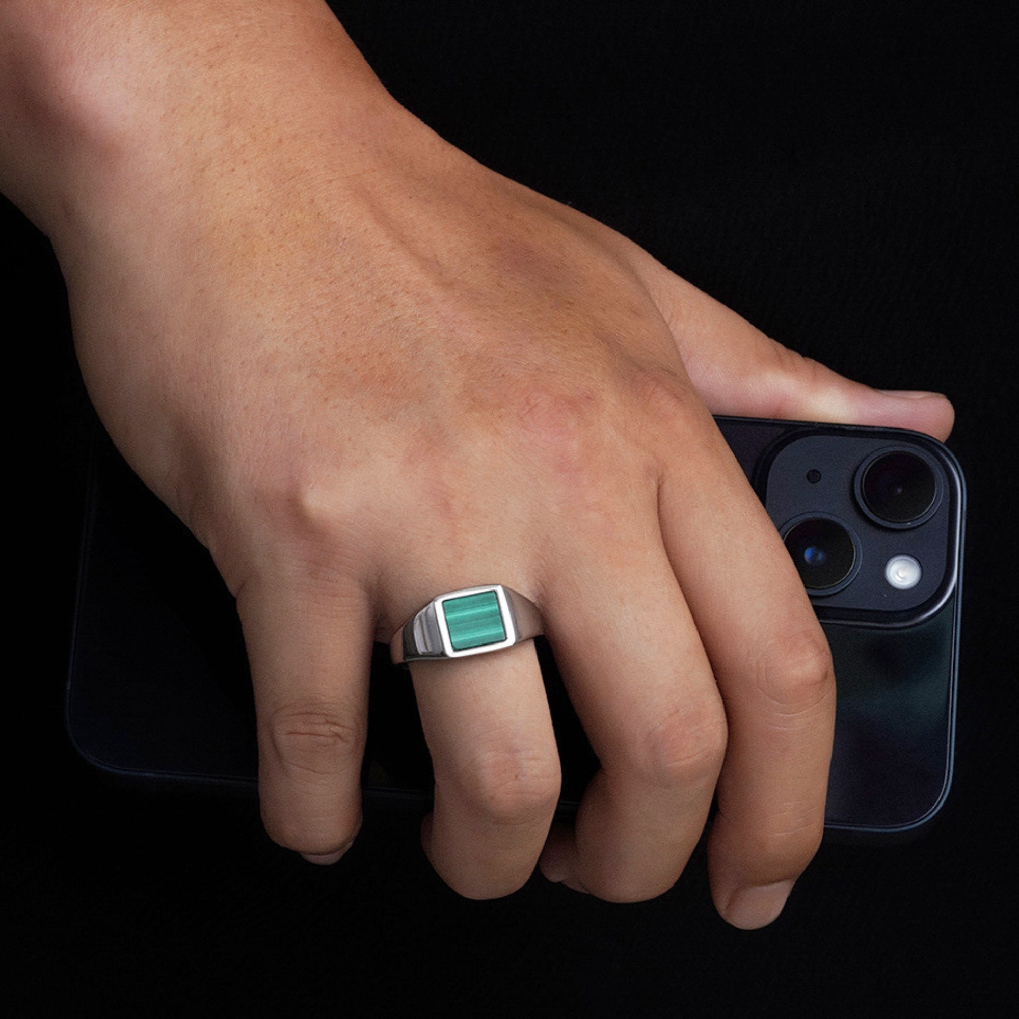 Hand wearing a ring holding a smartphone on a black background