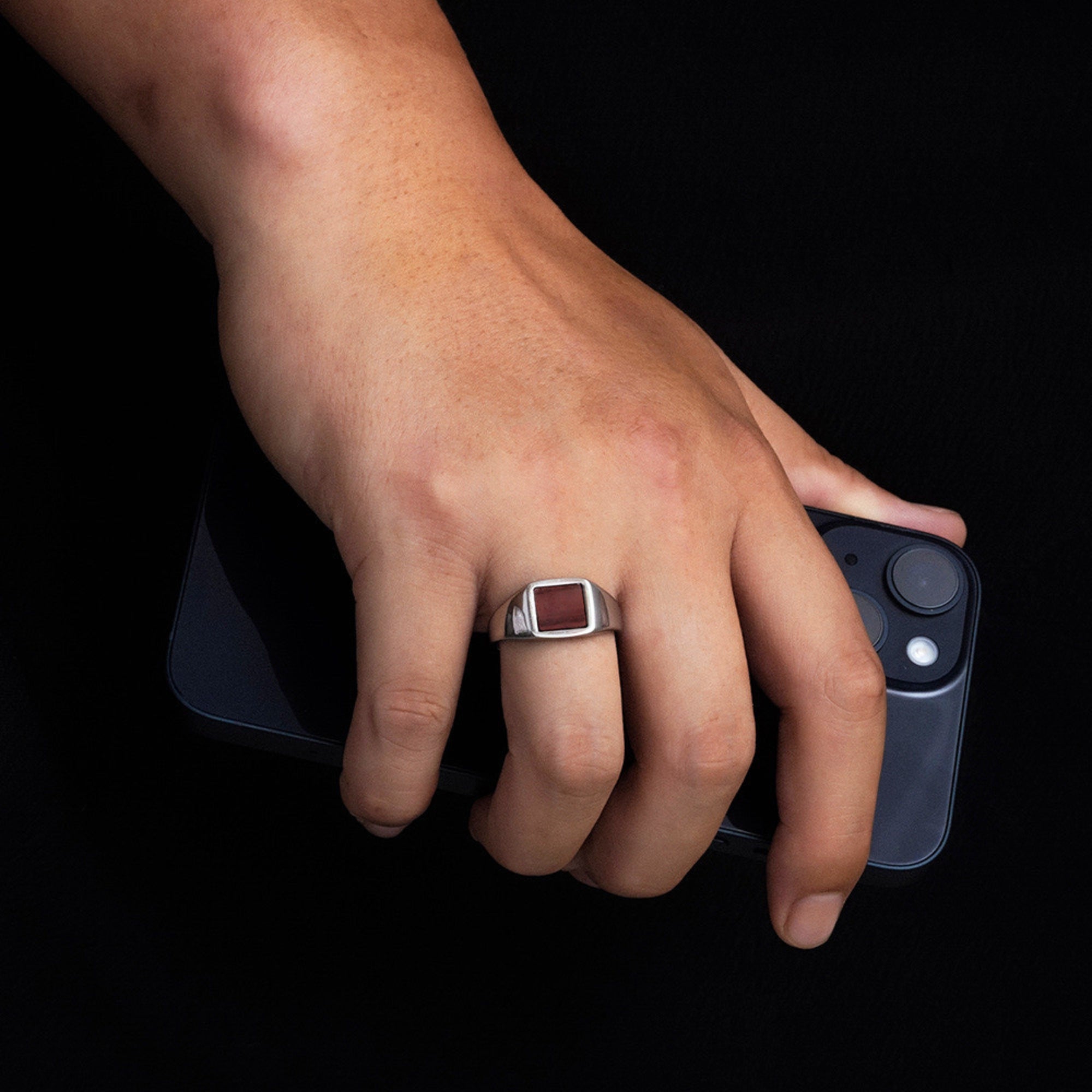 Hand wearing a ring holding a smartphone with a black background