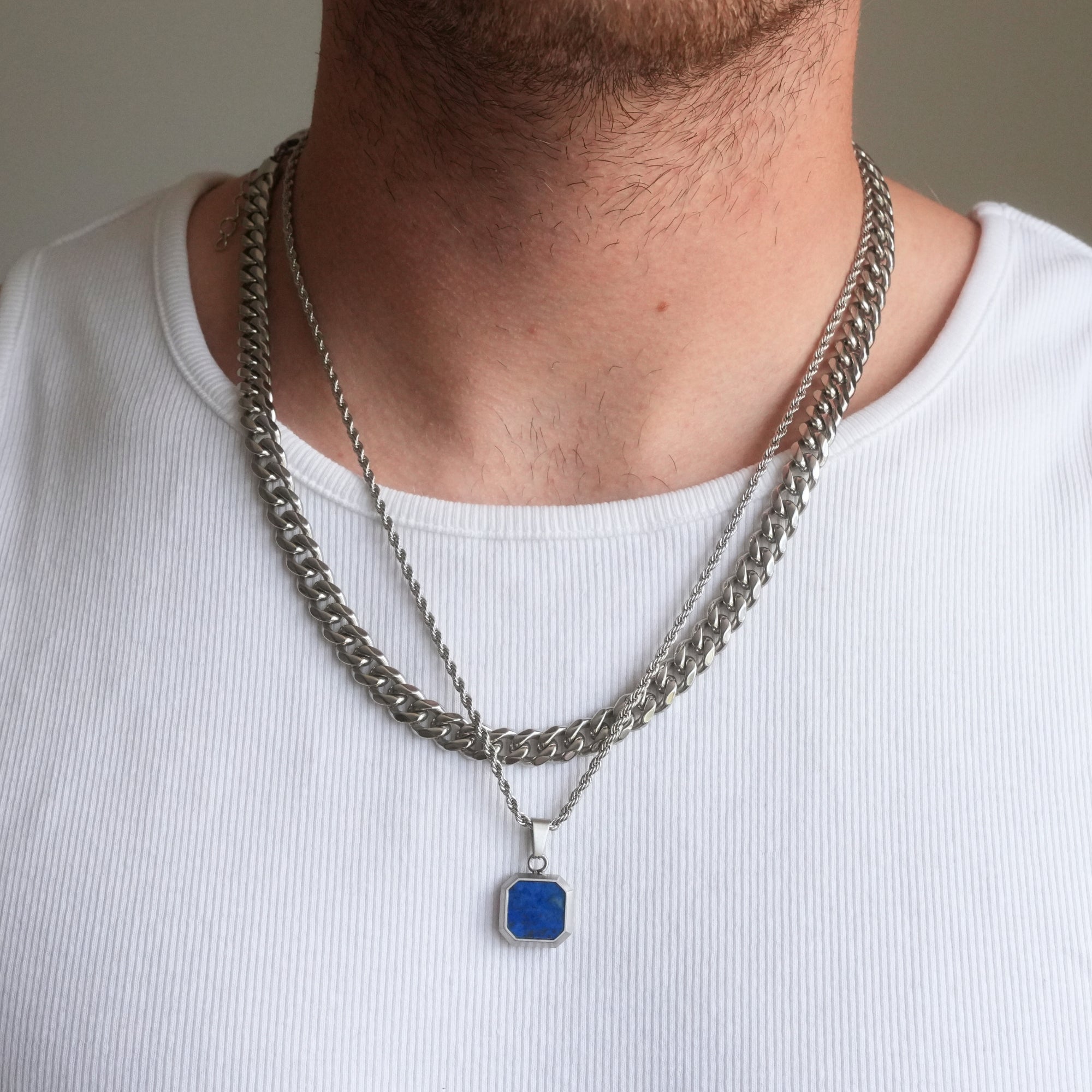 Person wearing a white shirt with two silver chain necklaces, one featuring a blue pendant.
