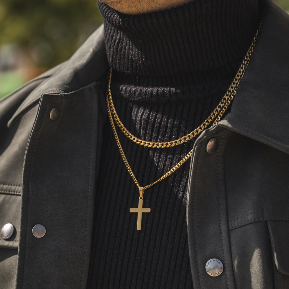 Person wearing a black turtleneck and leather jacket with gold chain necklaces, including a cross pendant.