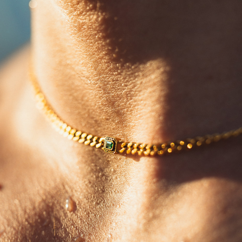 Gold anklet with a green gemstone on a person's ankle against a blurred background