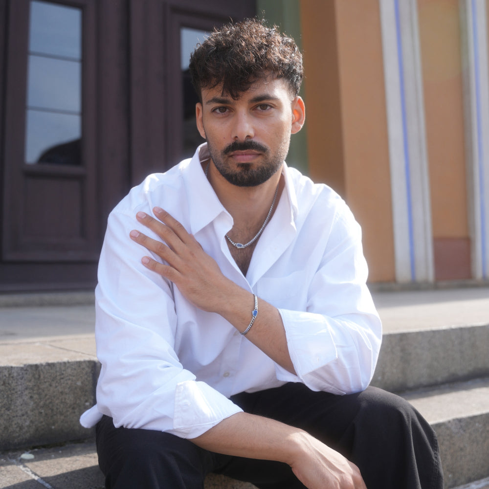Man wearing a white shirt sitting outdoors with a building in the background