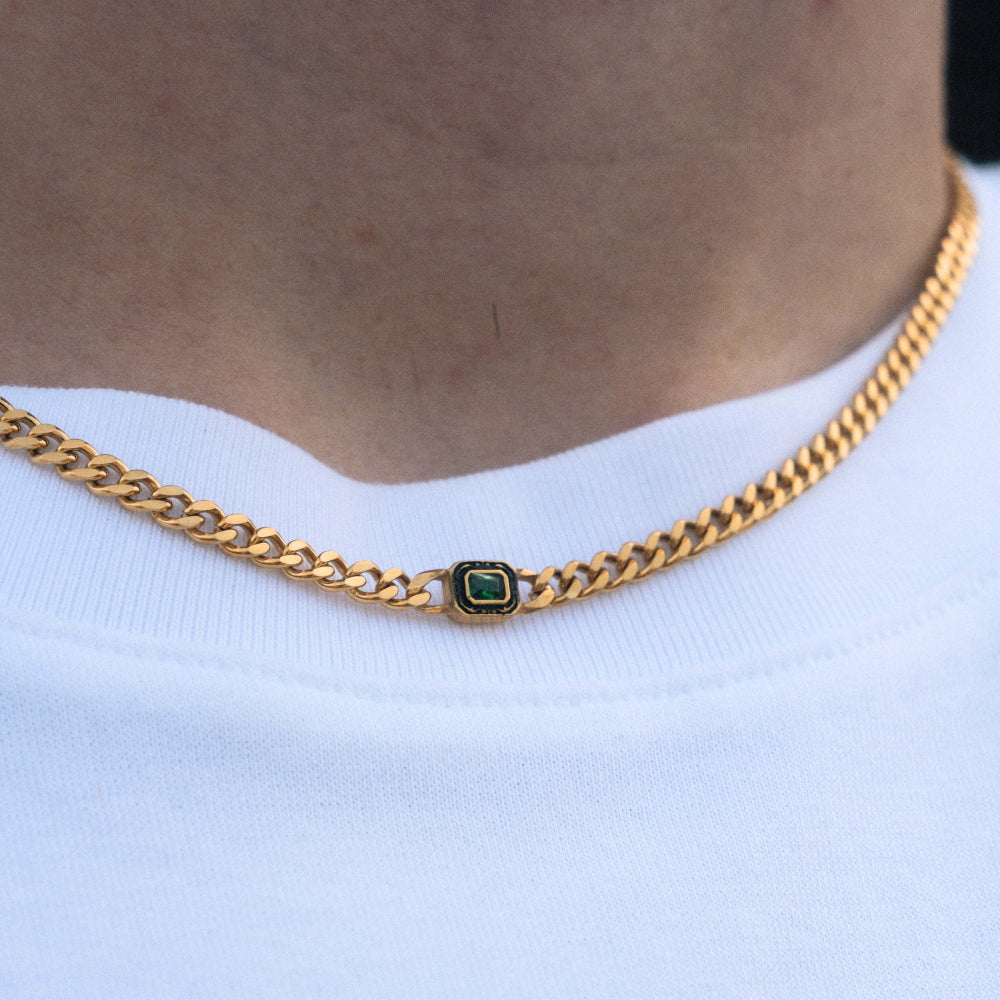 Gold chain necklace with a green gemstone on a white shirt