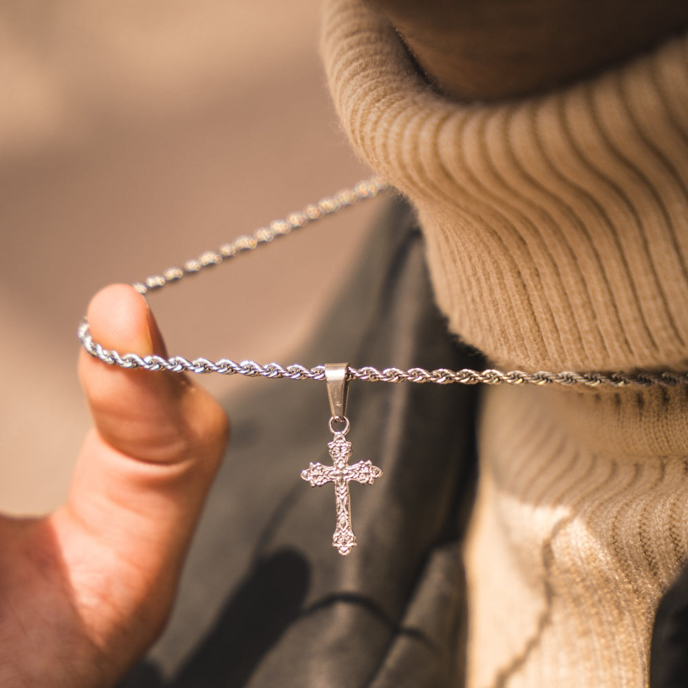 Silver cross necklace held by a hand with a blurred background