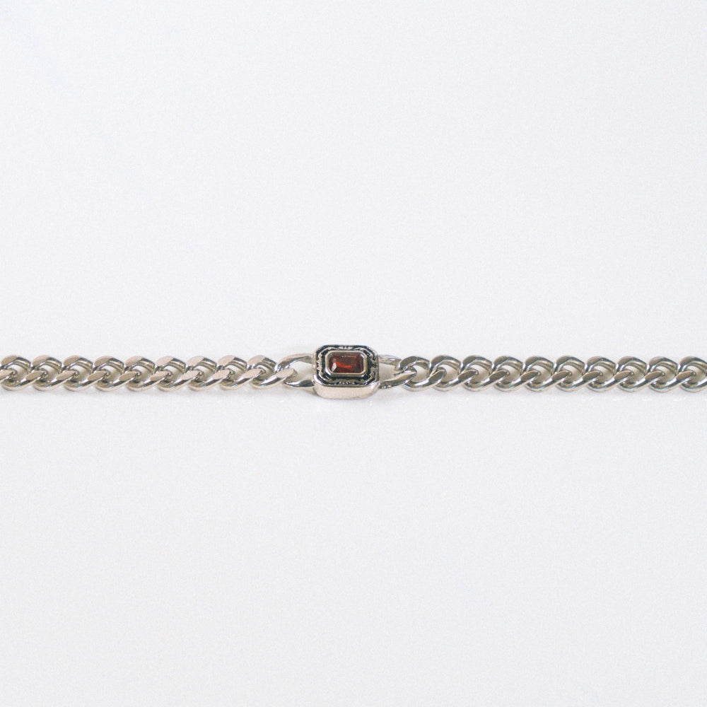 Silver chain bracelet with a red gemstone clasp on a white background