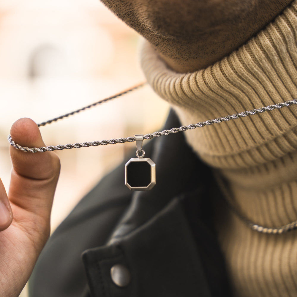Person wearing a silver necklace with a square pendant, blurred background