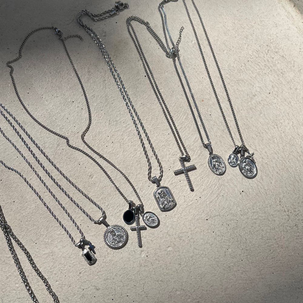 Collection of silver necklaces with various pendants on a light gray surface